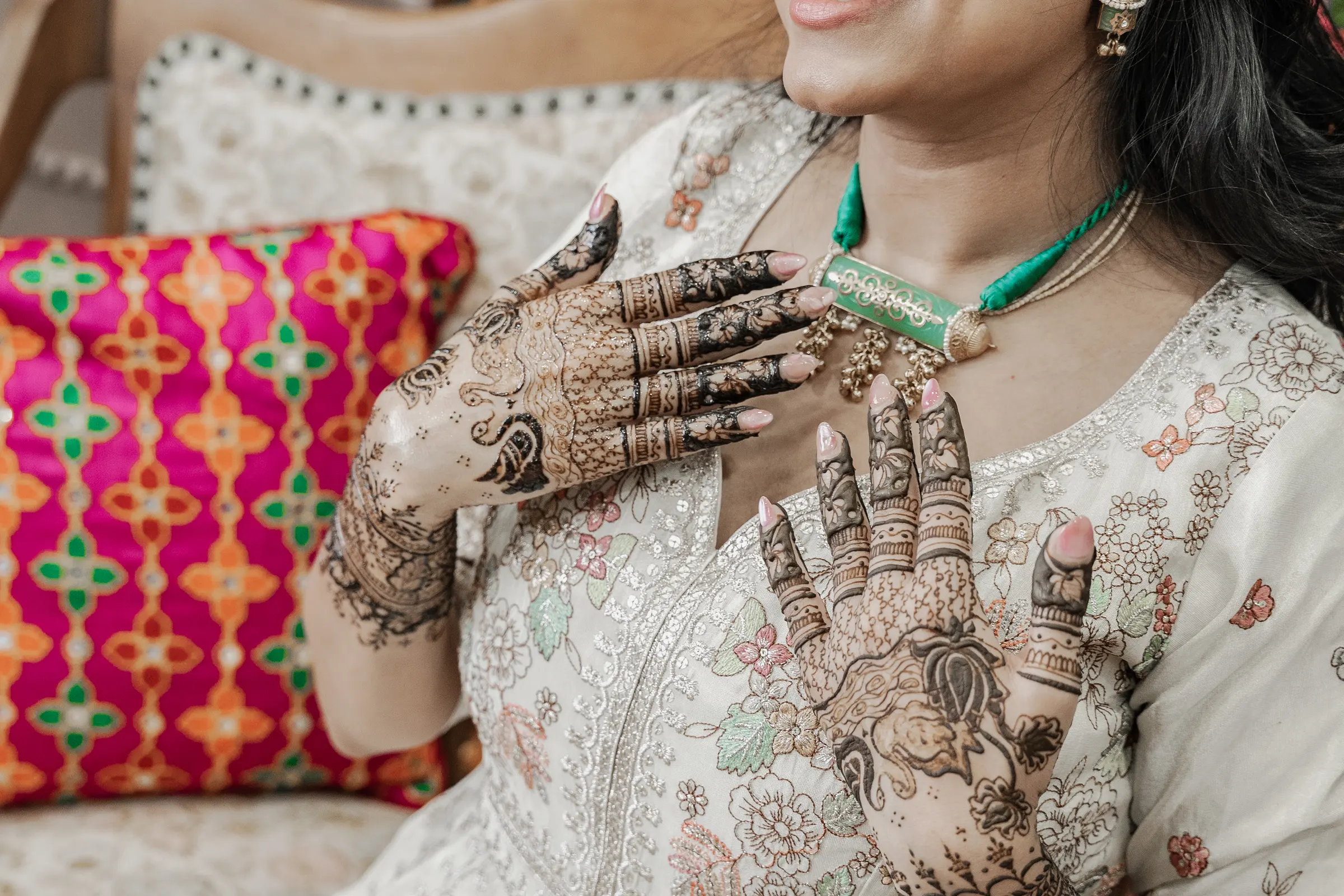 Two mehendi-covered hands resting against a bright printed cushion.