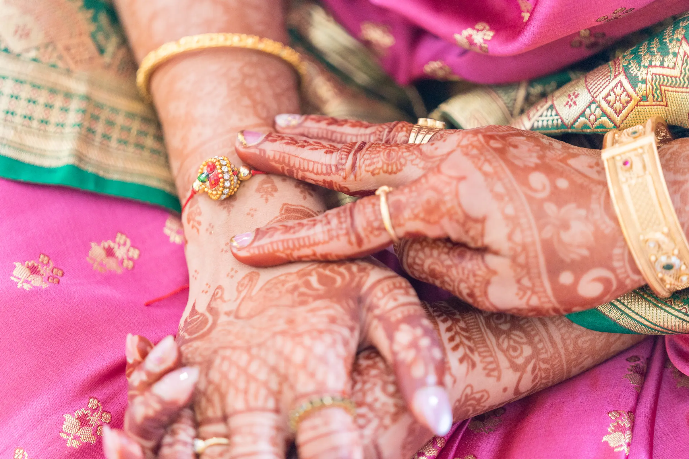 Mehendi-covered hands resting on a pink saree.