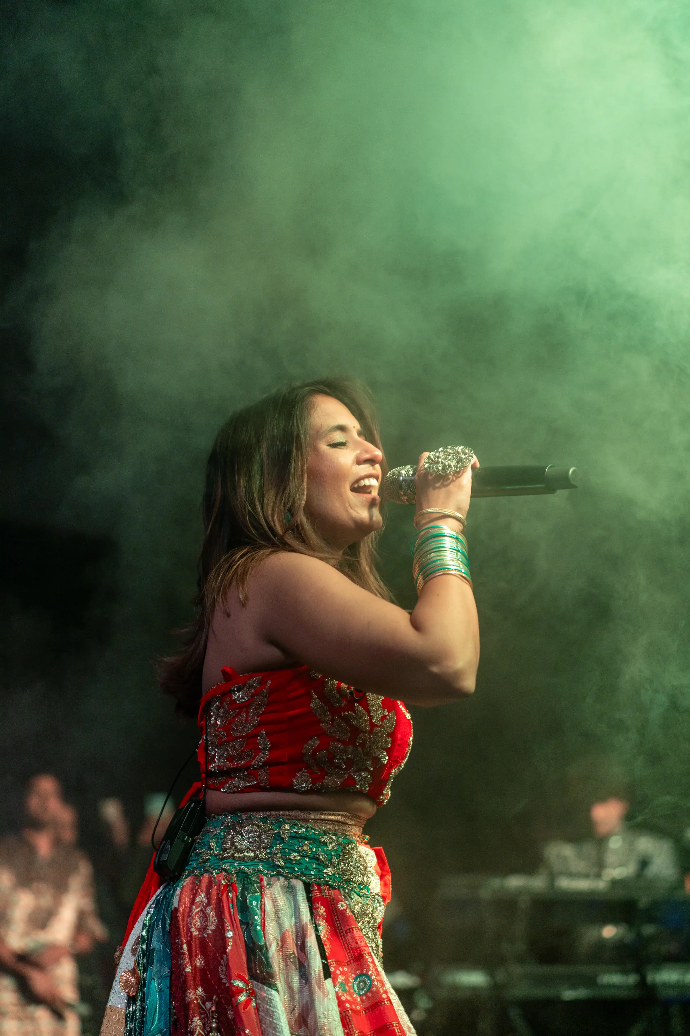 A singer mid-phrase on a stage filled with green haze and backlight.
