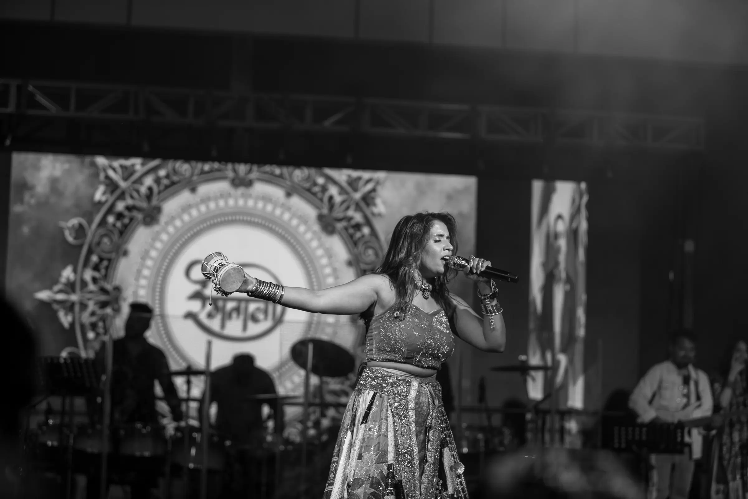 A singer performing in front of a lit stage backdrop, black and white.