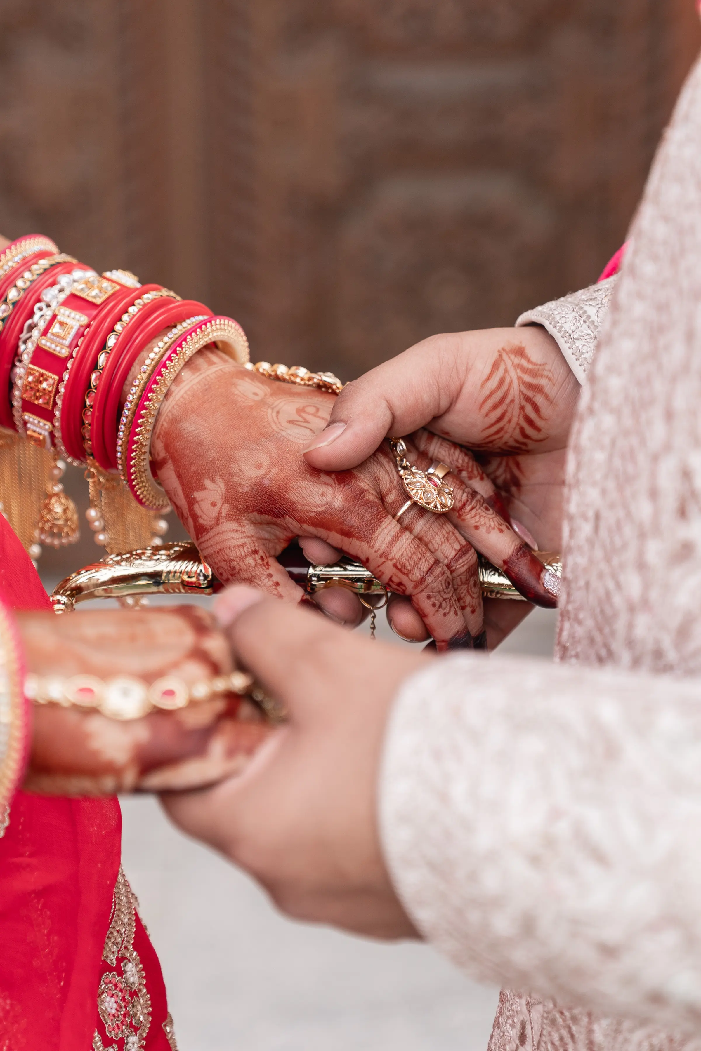 Close-up of a ring exchange, the bride’s mehendi-covered hands stacked with red and gold bangles.