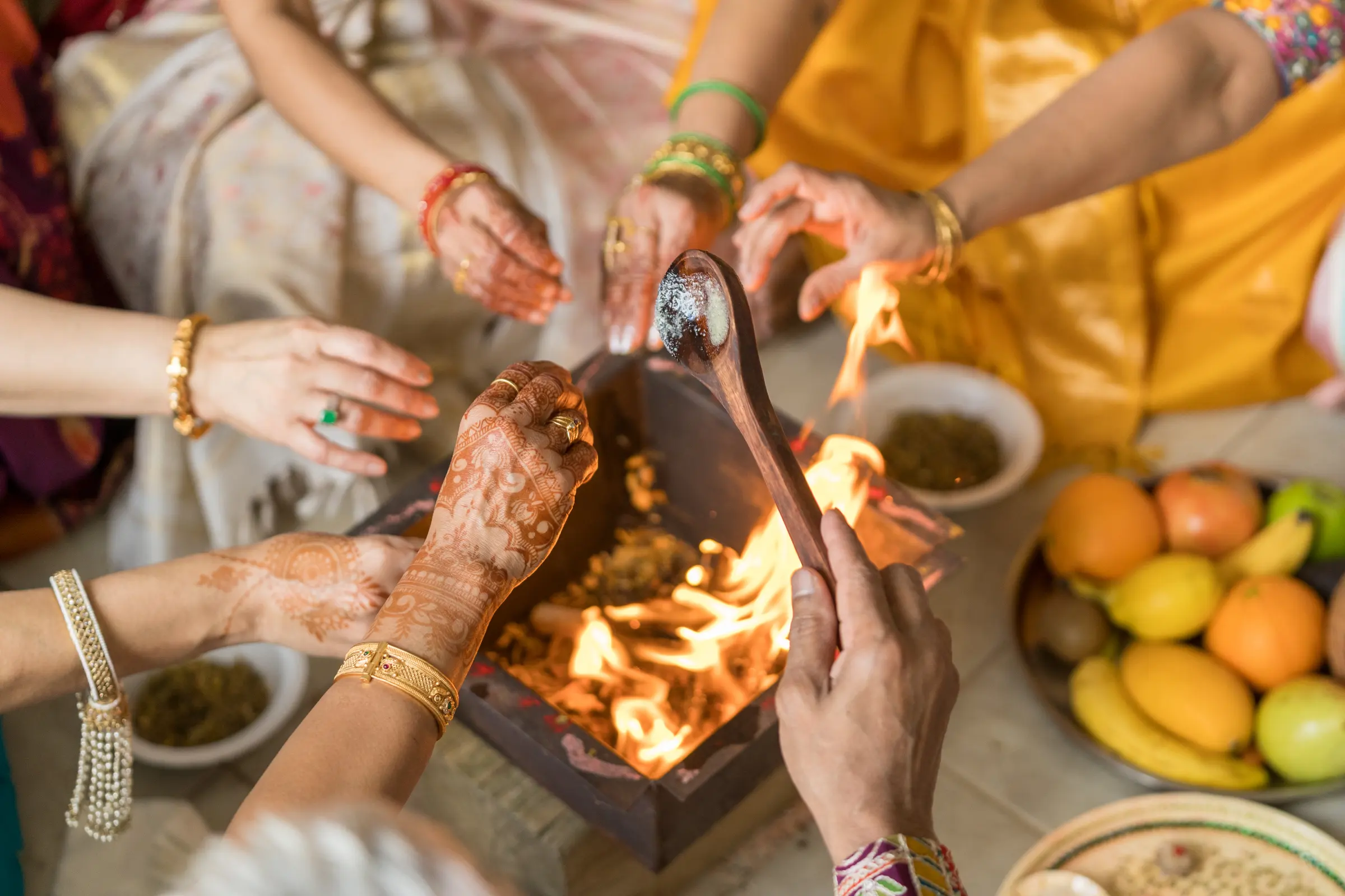 Hands make an offering into the ceremonial fire during the havan, a plate of fruit beside it.